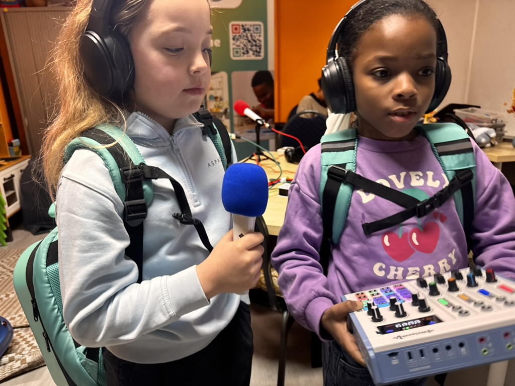 Twee leerlingen met rugzak dragen de WeSpeak-mixer en microfoon door de school